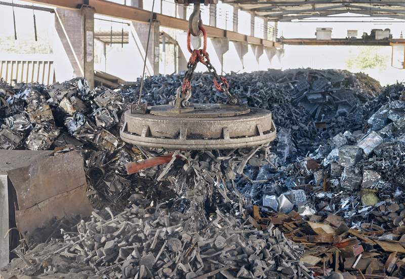 Magnetic crane lifting shredded metal scrap inside an industrial recycling facility in Vancouver, BC